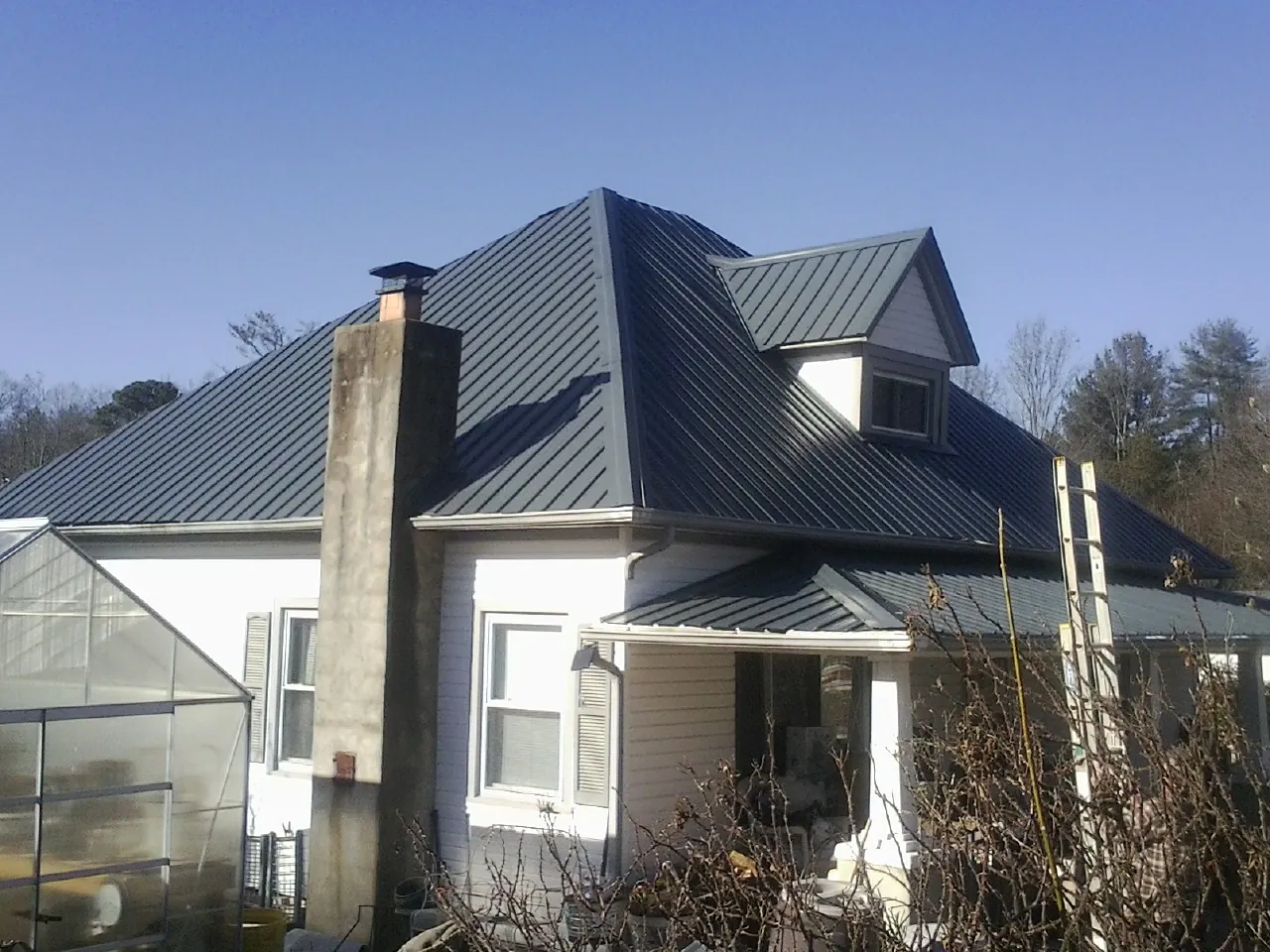 Dark blue standing seam metal roof on a white farmhouse with dormer — Slate & Tile Roof Repair by Roofing Brothers in Dillsboro