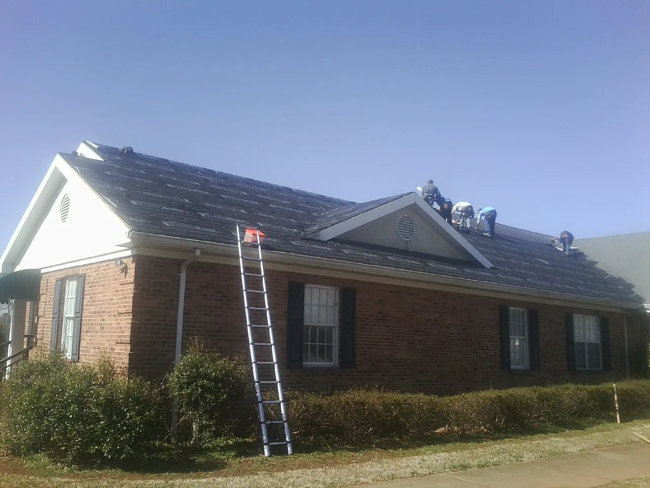 Crew tearing shingles off a brick ranch roof with a ladder set — Metal Roof Repair work by our crew in Dillsboro