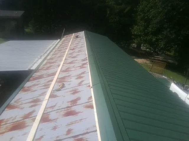 Old rusted panels beside newly installed green metal roofing — Wind Damage Roof Repair by Roofing Brothers in Dillsboro