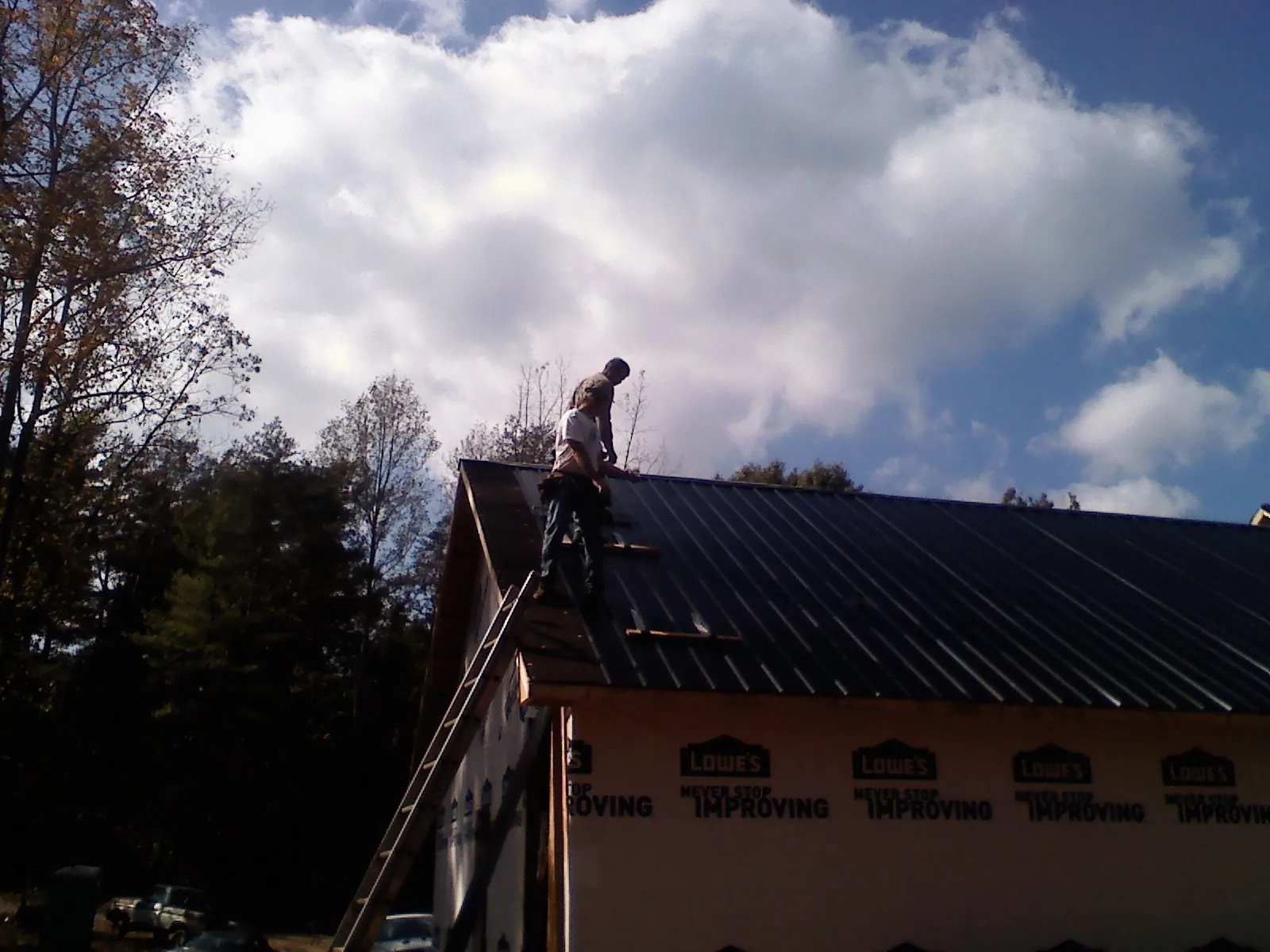 Roofer fastening dark metal panels high against a cloudy sky, from a Roof Inspection job in Dillsboro