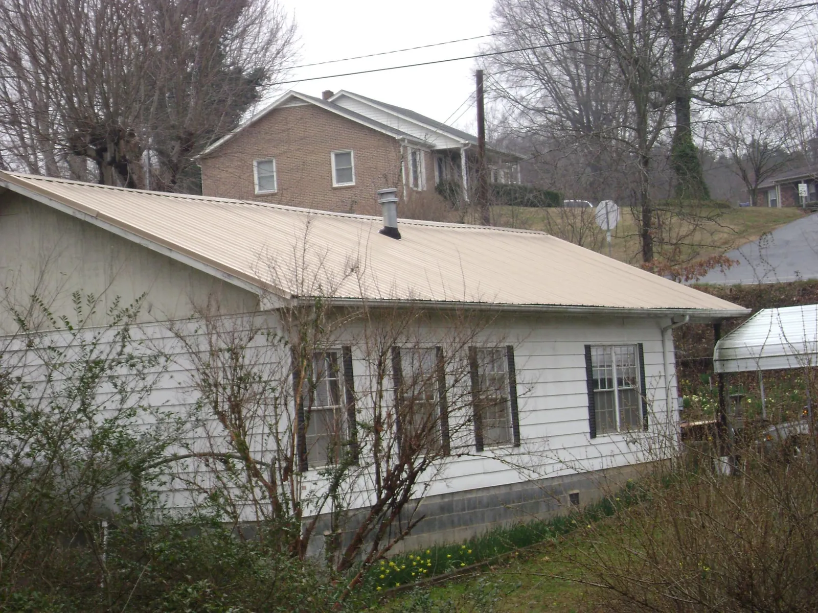 Tan metal roof on a white sided house set into a hillside — Commercial Roofing by Roofing Brothers in Dillsboro